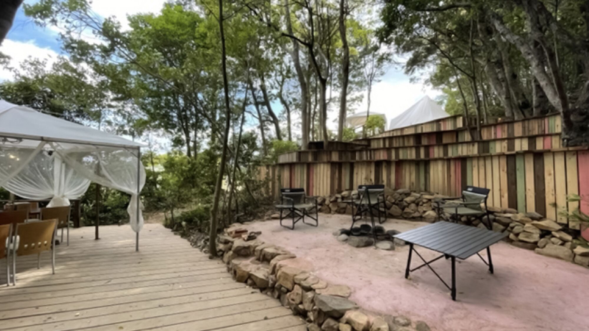 Eine Terrasse im Freien mit weißem Baldachin, Holzdeck und einer Sitzecke mit Stühlen und Tisch.