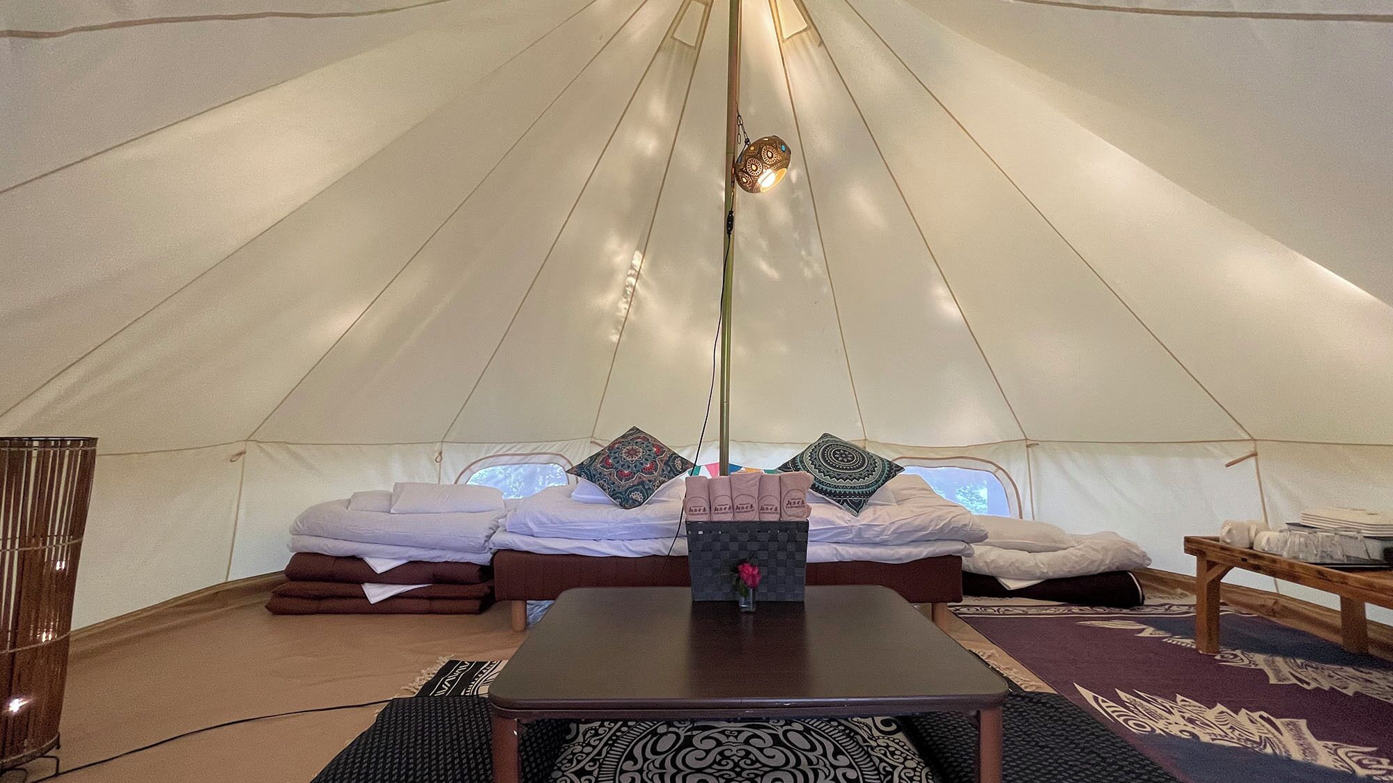 Ein Zelt mit Bett, Tisch und einer Hängelampe.