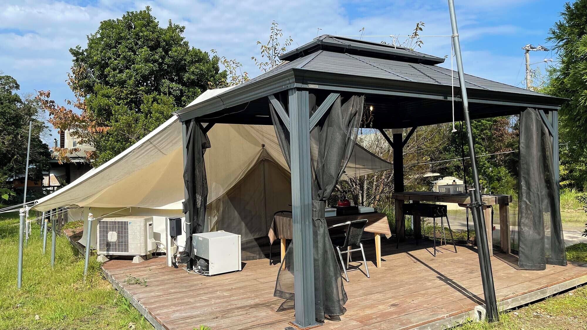 Ein überdachter Außenbereich mit Tisch, Stühlen, einem Grill und einer Klimaanlage.