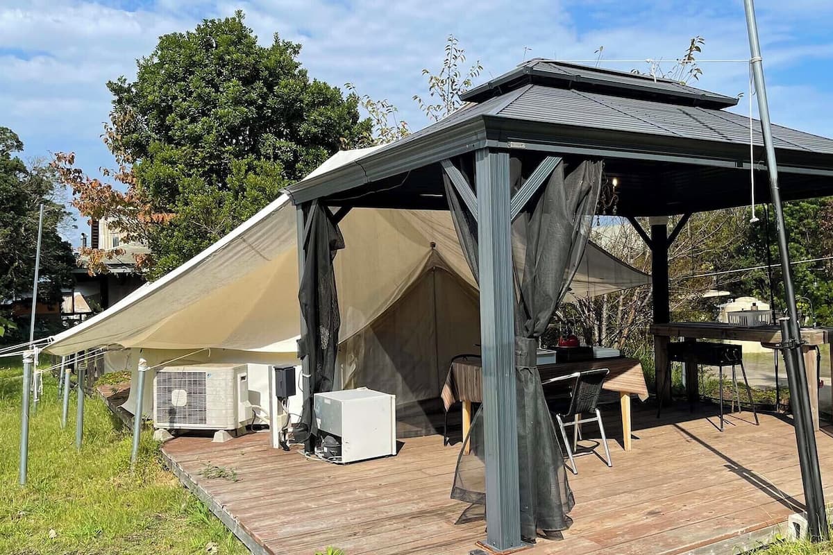 A covered outdoor area with a table and chairs, a grill, and an air conditioning unit.
