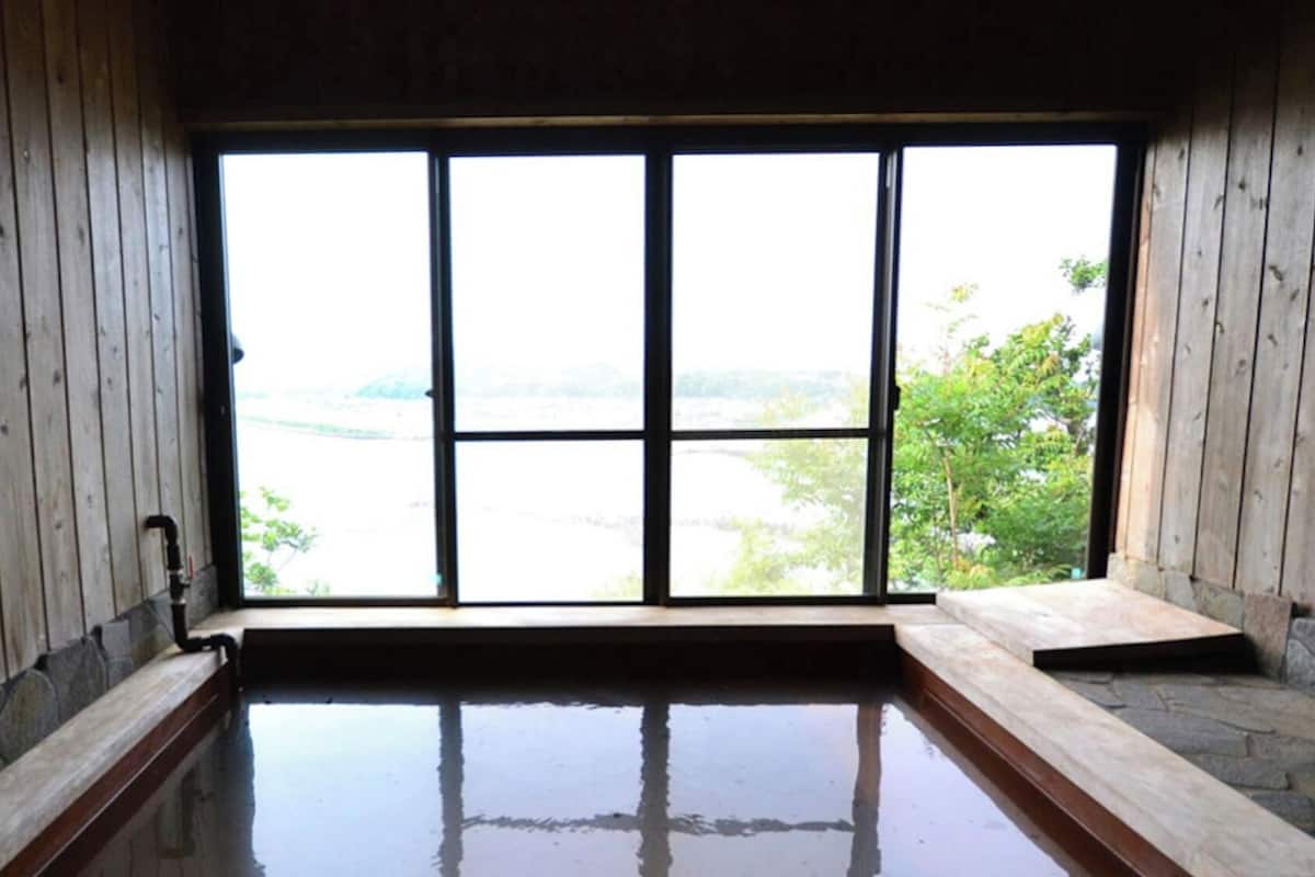 A wooden room with a large window, a stone bench, and a small pool.
