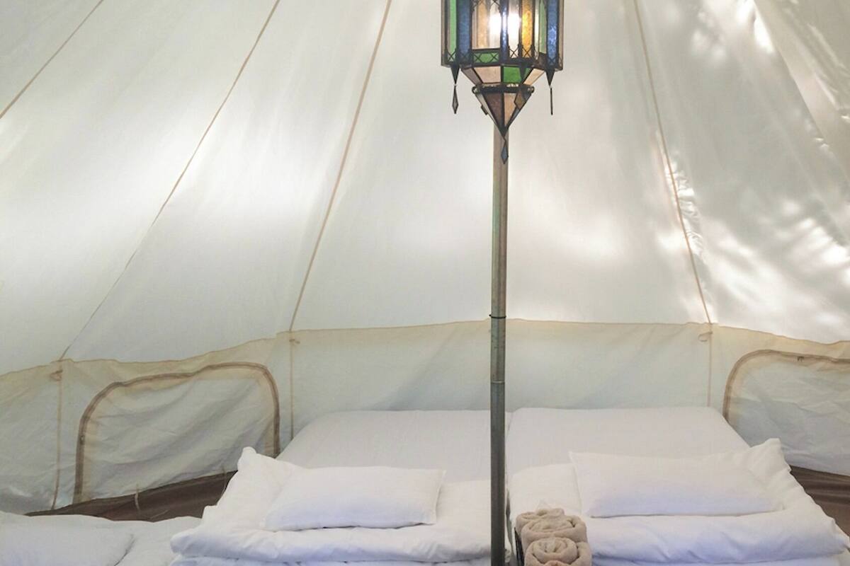 A tent with two beds, a central pole, and a hanging light fixture.