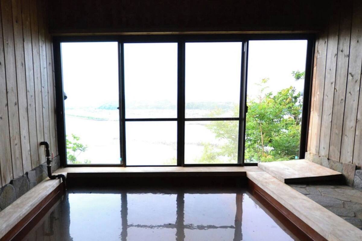A wooden room with a large window, a stone bench, and a small pool.