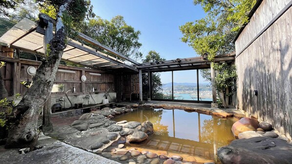 A traditional Japanese onsen with a stone bath surrounded by wooden structures and a view of the landscape.