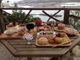 Una mesa de madera con varios platos y vistas al paisaje costero.