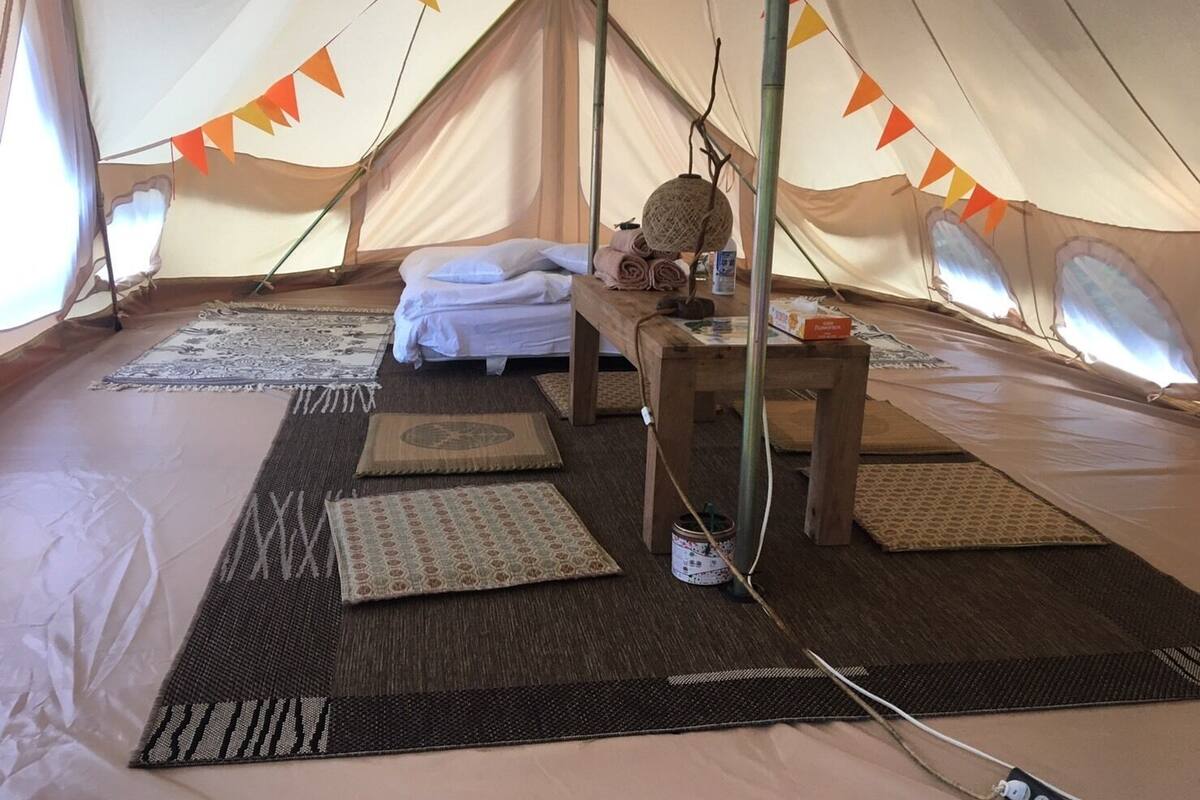 A tent with a bed, pillows, a table, and mats on the floor.