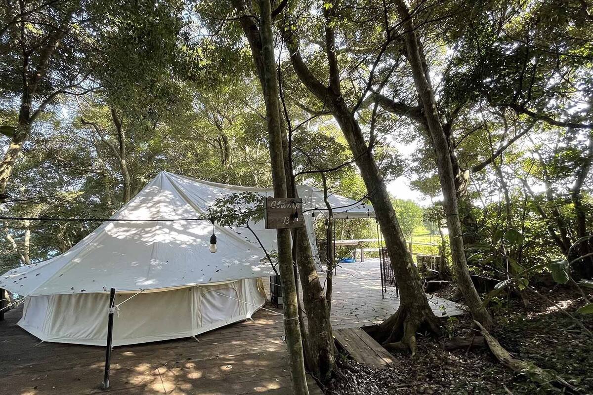 A large tent in a forested area with a sign indicating 'Lodge 13'.