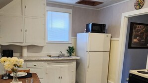 A compact kitchen with white cabinets, a refrigerator, a microwave, and a dining area with a wooden table and chairs. - Large spacious room 5 minutes walk to historic downtown Manistee (Manistee)