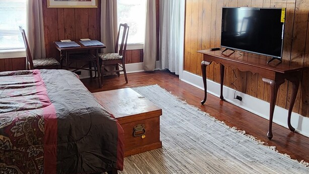 A hotel room with a bed, a TV, a wooden panel wall, a painting, and a window with curtains. - Large spacious room 5 minutes walk to historic downtown Manistee (Manistee)