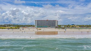 A beachfront hotel with multiple floors, a sandy beach in the foreground, and a clear sky. - Stunning direct oceanfront views from your own balcony! (Daytona Beach)