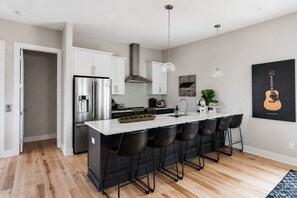 A modern kitchen with a central island, stainless steel appliances, and black bar stools. - Modern Rooftop Retreat • Nashville Views (Nashville)