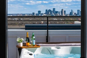 Un balcón con un jacuzzi, una bandeja con dos botellas y vista al horizonte de la ciudad.
