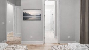 A hallway with a framed landscape painting, a door leading to another room, and a bed with a patterned bedspread. - Modern Rooftop Retreat • Nashville Views (Nashville)