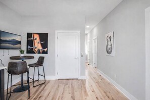 Un couloir avec un coin repas comprenant une table et des chaises, une porte blanche et des œuvres d’art accrochées aux murs.