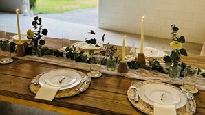 A long wooden table set for a meal with candles, glassware, and greenery.