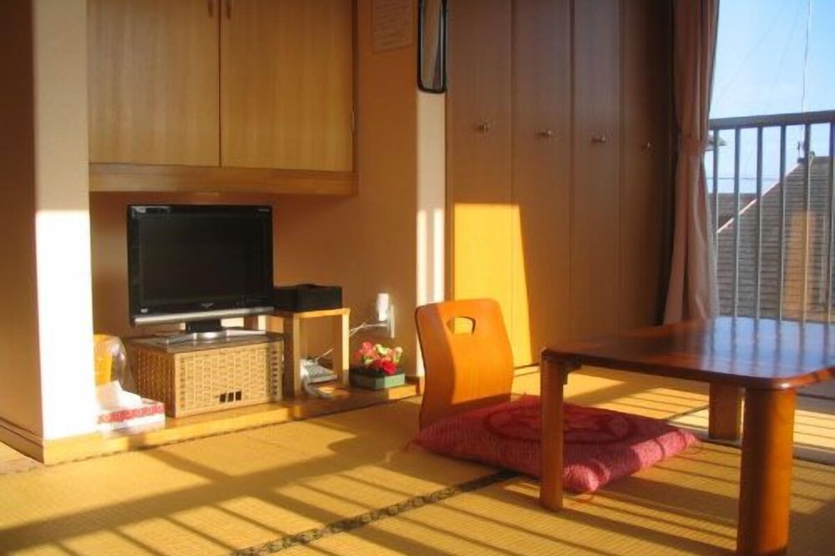 A room with a television, wooden cabinets, a dining table, and a view of the outside.