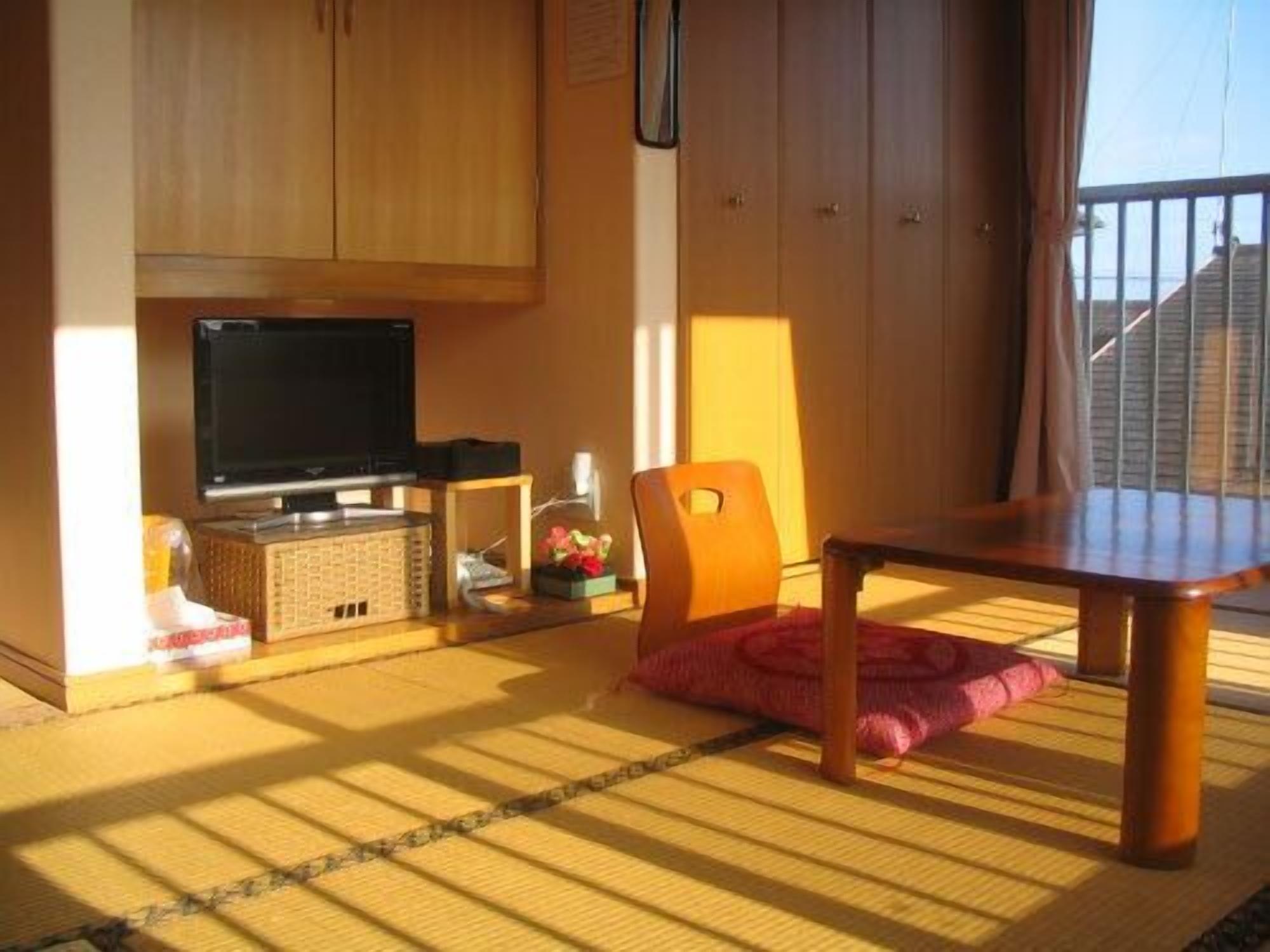 A room with a television, wooden cabinets, a dining table, and a view of the outside.