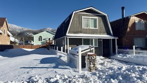 Un quartier résidentiel enneigé, avec une maison dotée d’un pilier en pierre, d’une clôture en bois et un ciel dégagé.
