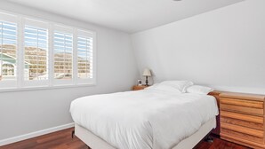 Une chambre à coucher avec un grand lit, des tables de chevet en bois, une lampe et une fenêtre avec des stores.