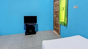 A room with a bed, a television on a stand, and a wooden door with a green curtain. - Spot On 91811 Rumah Inap Bunda Nurhayati (Tanak Awu)