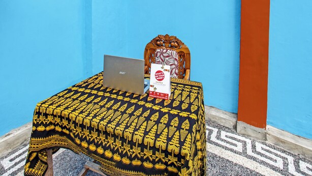 A room with a blue wall, a patterned tablecloth, a laptop, a decorative chair, and a poster on the wall. - Spot On 91811 Rumah Inap Bunda Nurhayati (Tanak Awu)