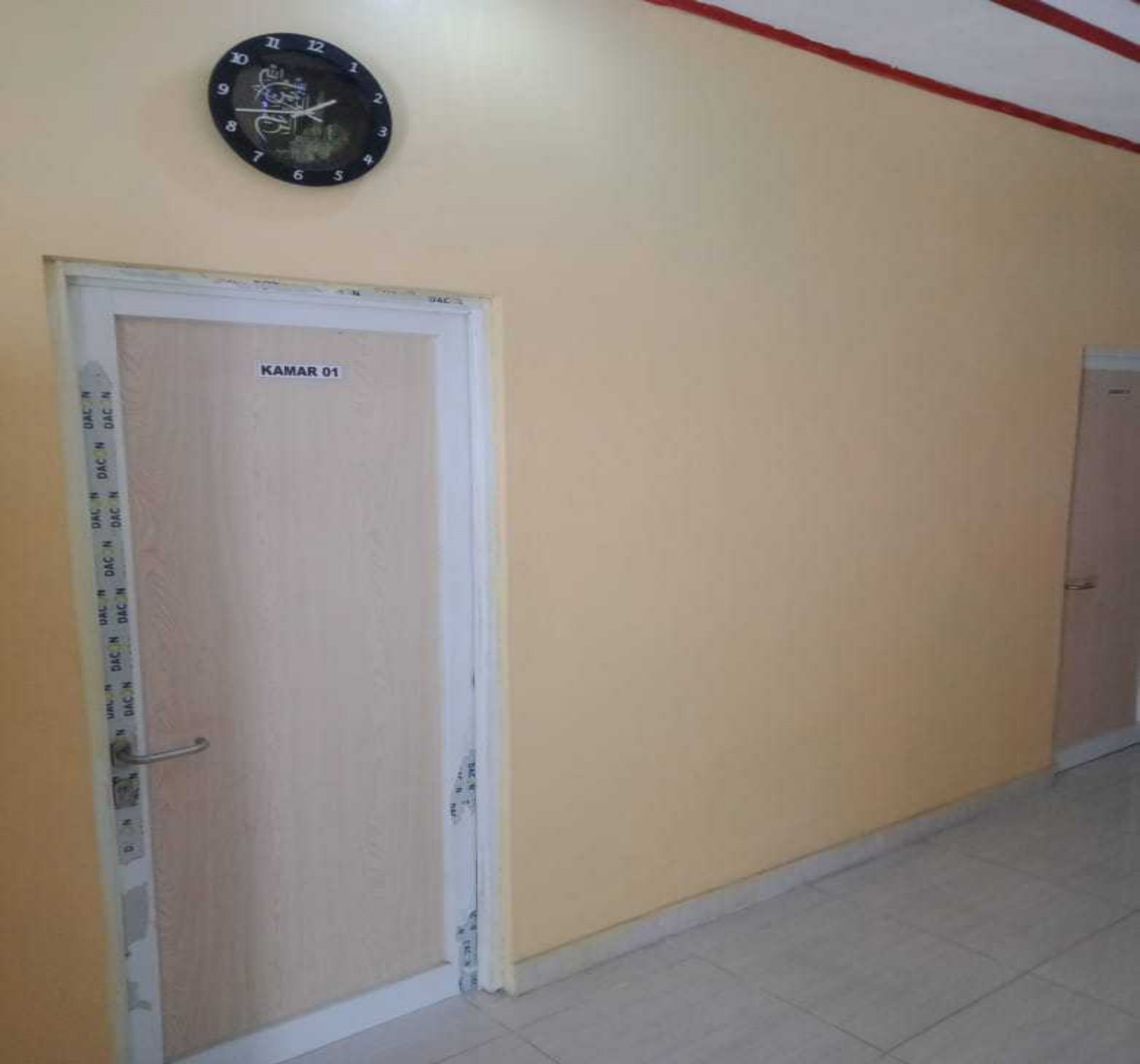 A hallway with a door labeled 'KAMAR 01' and a wall clock above it.