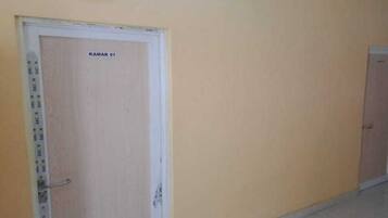 A hallway with a door labeled 'KAMAR 01' and a wall clock above it.