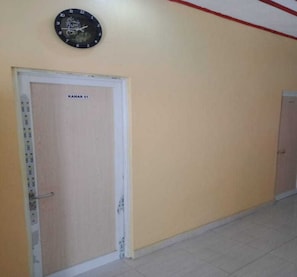 Un pasillo con una puerta que indica 'KAMAR 01' y un reloj de pared encima.