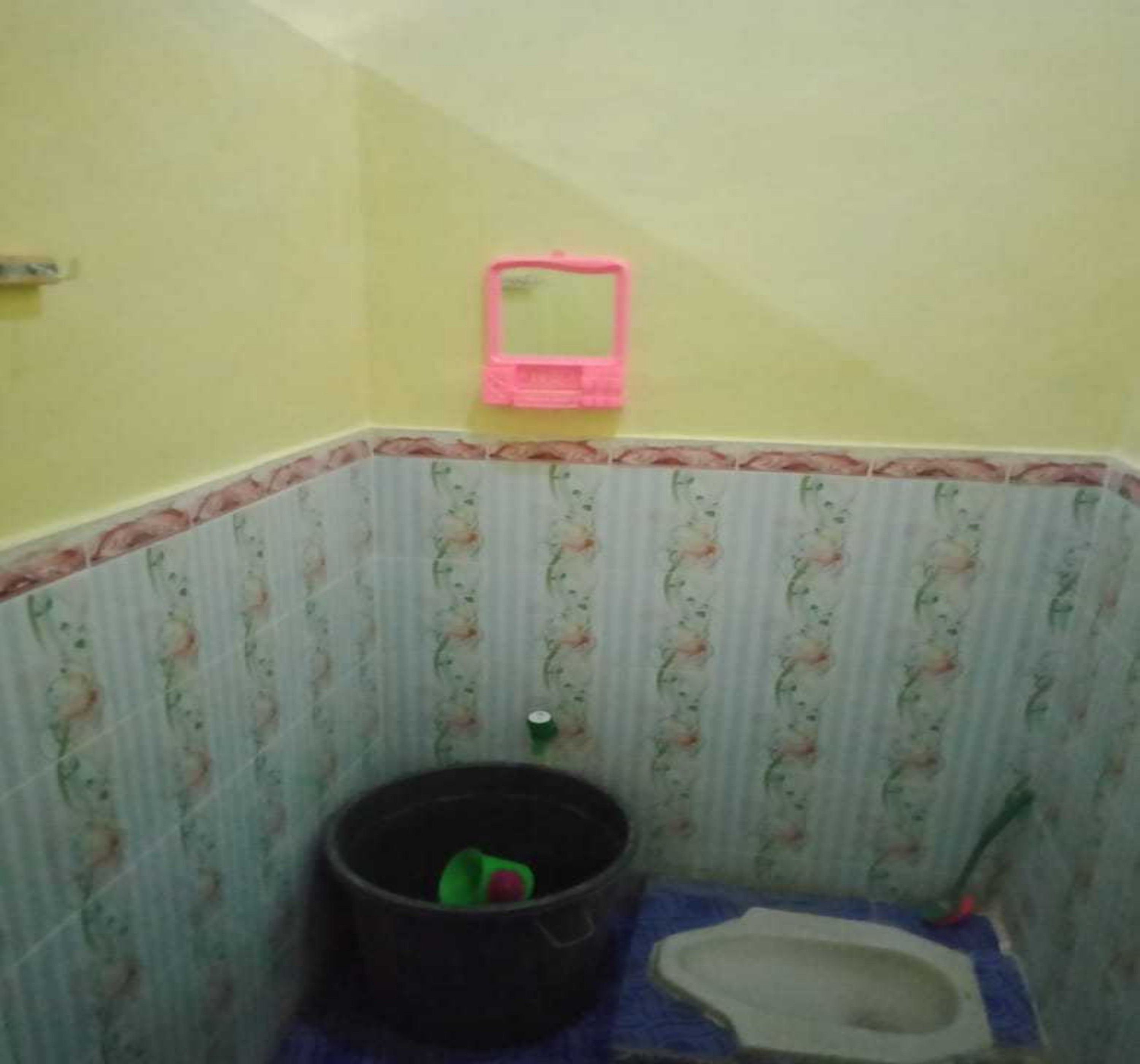 Een kleine badkamer met toilet, een emmer en een spiegel aan de muur.