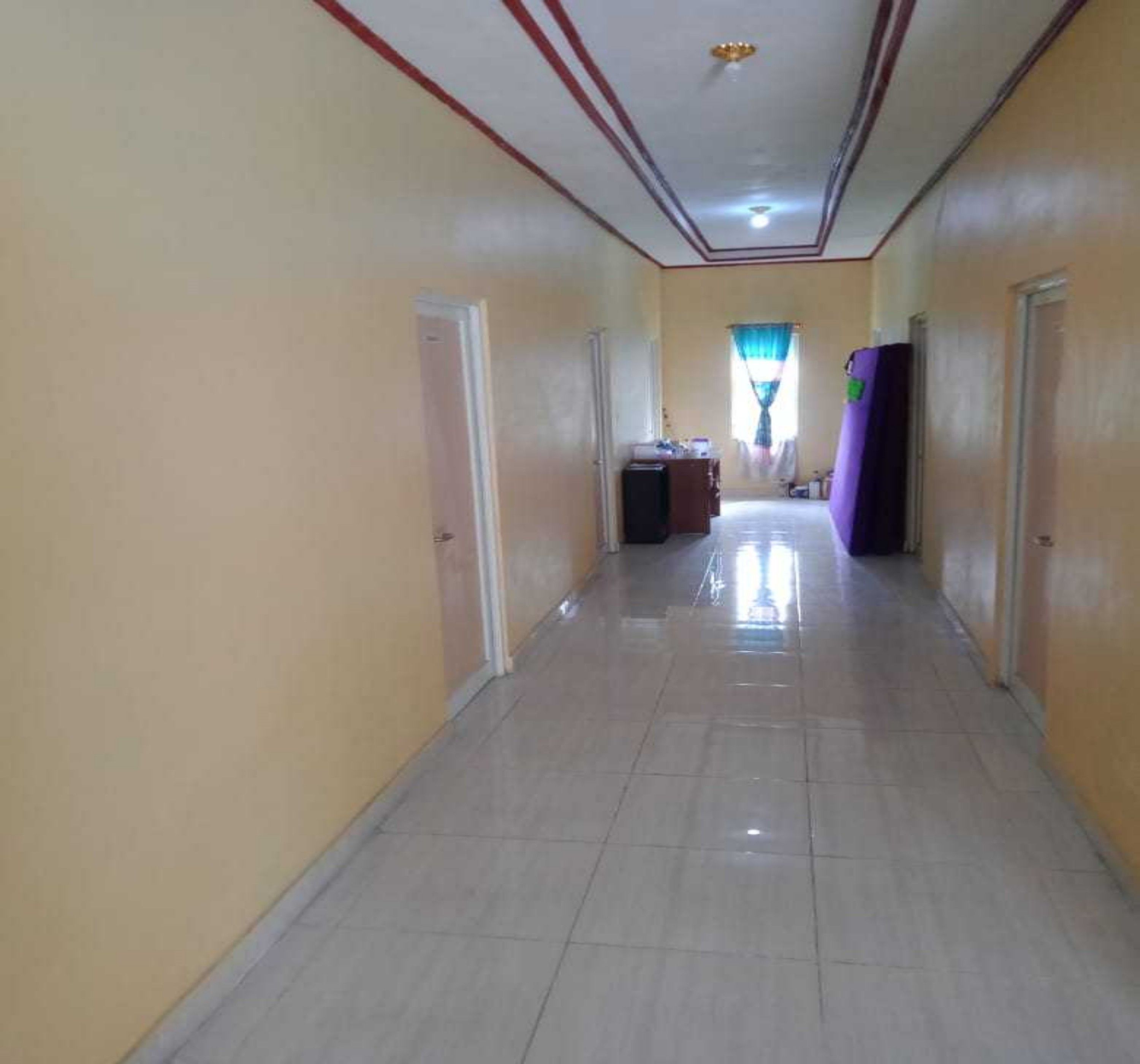 A hallway with a tiled floor, doors on both sides, and a window with curtains at the end.