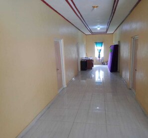 A hallway with a tiled floor, doors on both sides, and a window with curtains at the end. - Express O 91371 Wisma Nadira (Pesisir Utara)