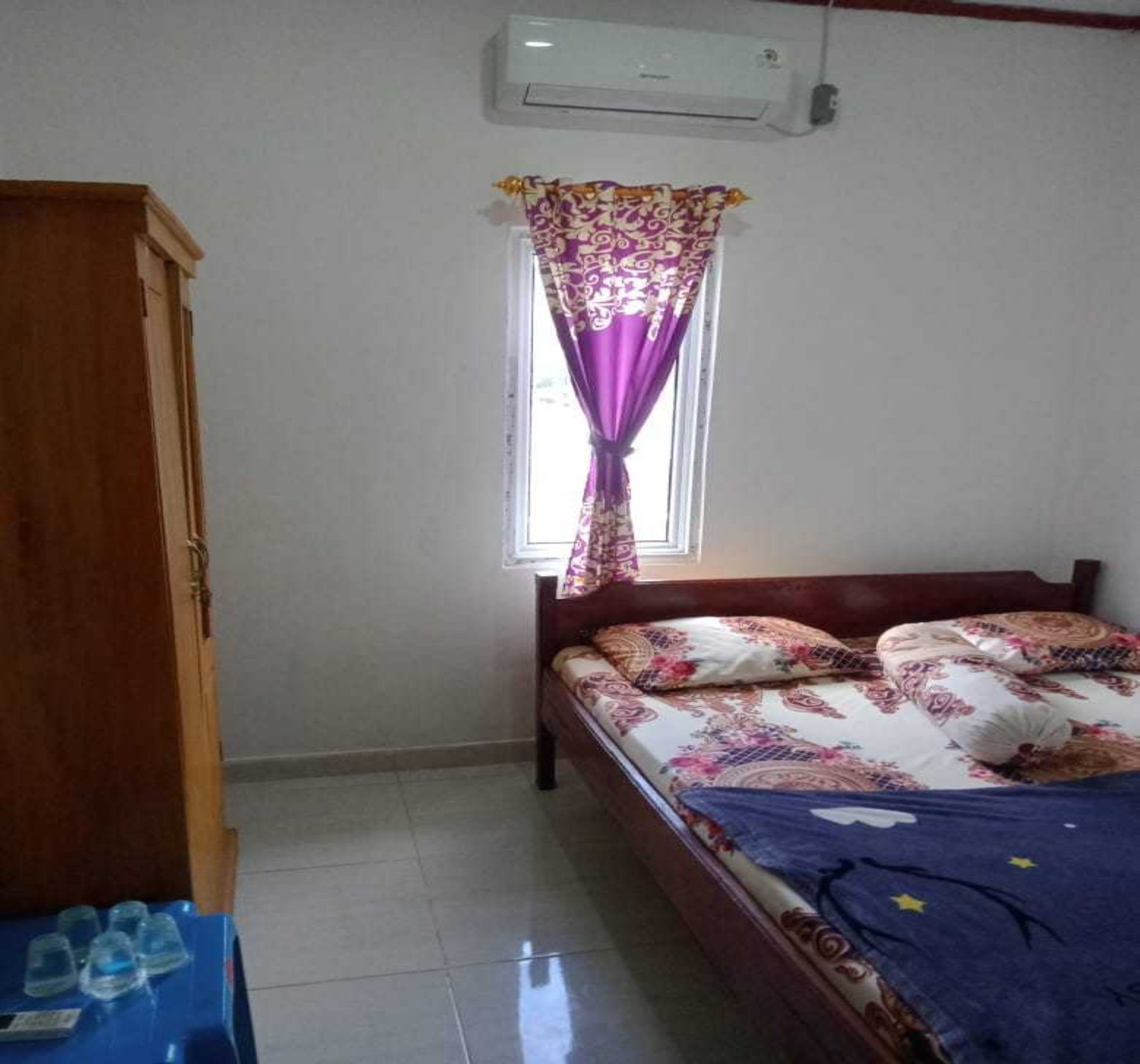 Un dormitorio con cama, armario, ventana con cortinas y unidad de aire acondicionado.