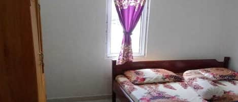 A bedroom with a bed, a wardrobe, a window with curtains, and an air conditioning unit.