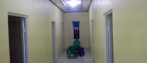 A narrow hallway with doors on both sides, a ceiling light, and a window with blue curtains.