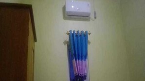 A room with a ceiling-mounted air conditioner, a door, and a curtain rod with a curtain.