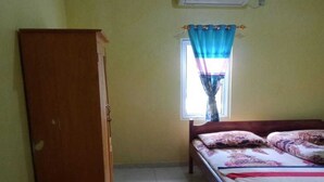 A small, simple room with a bed, a wardrobe, and a window with curtains.
