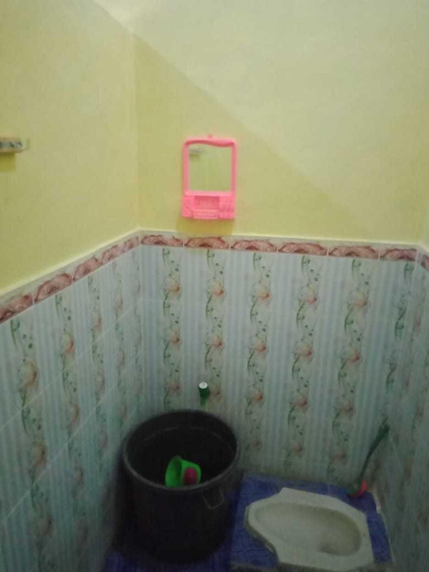 A small bathroom with a toilet, a trash bin, and a pink mirror.