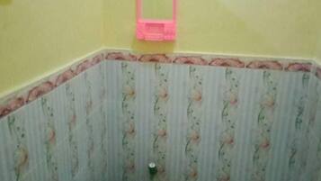 A small bathroom with a toilet, a trash bin, and a pink mirror.
