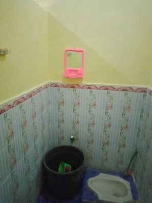 Un baño pequeño con inodoro, un cesto de basura y un espejo rosa.