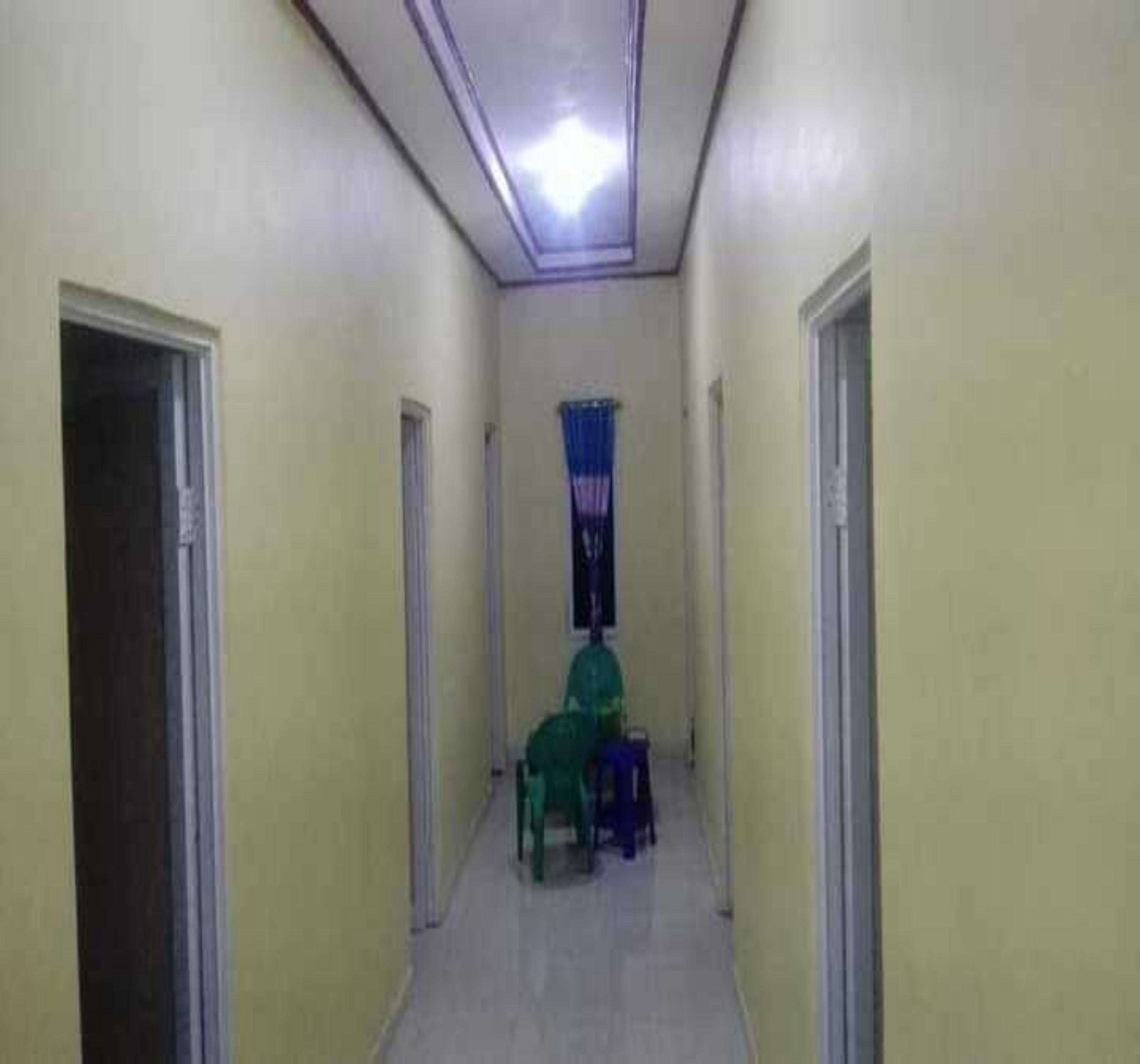 A narrow hallway with doors on both sides, a ceiling light, and a window with blue curtains.