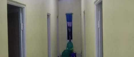 A narrow hallway with doors on both sides, a ceiling light, and a window with blue curtains.