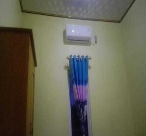 A room with a ceiling-mounted air conditioning unit, a door on the left, and a curtain rod with a curtain. - Express O 91371 Wisma Nadira (Pesisir Utara)