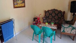 A living room with a sofa, two turquoise chairs, a small table with a few items, a red bicycle, and a painting on the wall.
