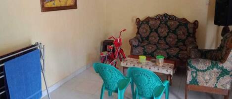 A living room with a sofa, two chairs, a table with a tablecloth, a painting on the wall, and a blue mat on the floor.