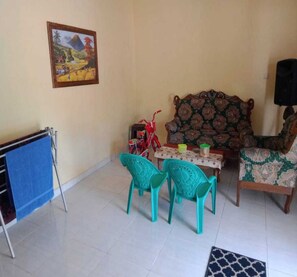 Een woonkamer met een bank, twee turquoise stoelen, een klein tafeltje met enkele spullen, een rode fiets en een schilderij aan de muur.
