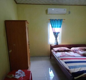 A bedroom with a bed, a wardrobe, a window with curtains, and an air conditioning unit. - Express O 91371 Wisma Nadira (Pesisir Utara)