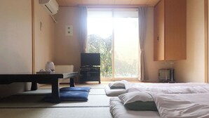 Habitación de hotel con cama, escritorio, televisor y puerta corrediza de vidrio al exterior.