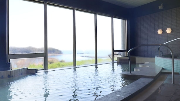 Una amplia piscina interior con vistas a un lago y montañas a través de grandes ventanales.
