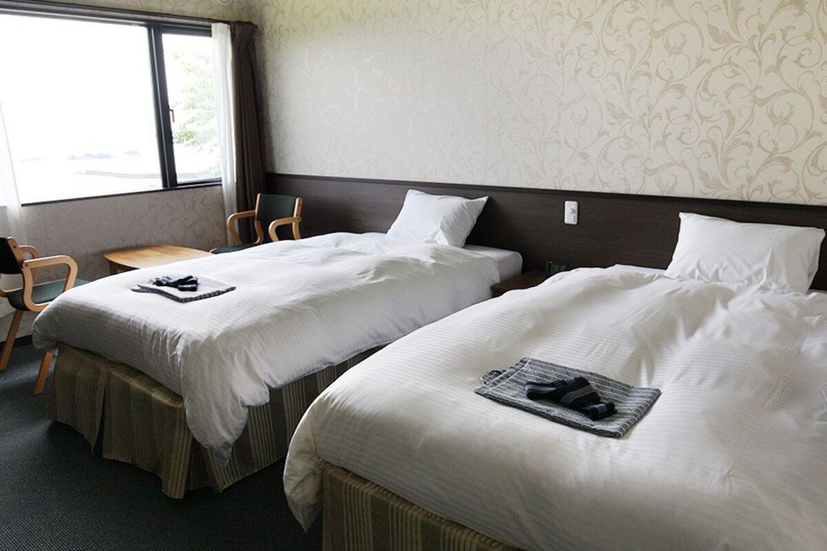 Una habitación de hotel con dos camas individuales, una mesita pequeña y una silla.