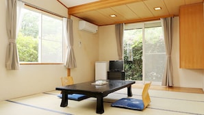 Una habitación con esteras de tatami, una mesa baja, un televisor y un fusuma que da a un jardín.